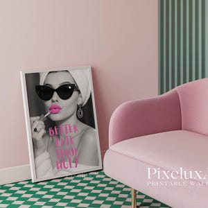 May include: Black and white framed print featuring a woman applying pink lipstick, wearing sunglasses and a headscarf. The text "Better Late Than Ugly" is displayed in pink. A pink velvet chair and a green and white checkered floor are also visible.