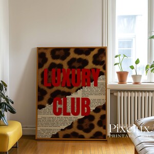 May include: A framed print featuring the words "LUXURY CLUB" in bold red letters against a leopard print background. The design incorporates torn paper elements, adding a textured effect. The artwork is displayed in a room with natural light.