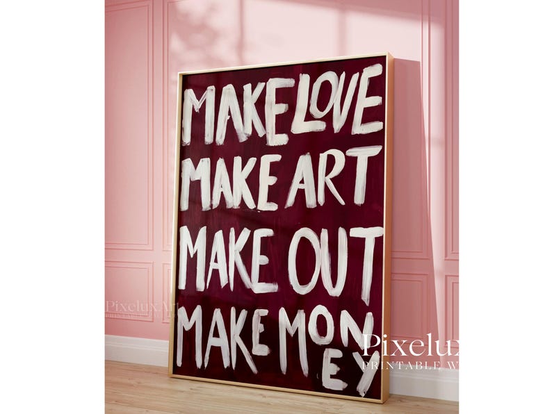 Puede incluir: Un cuadro rectangular en un marco dorado fino con un fondo color burdeos intenso y el texto pintado a mano en blanco: MAKE LOVE, MAKE ART, MAKE OUT, MAKE MONEY. Las letras tienen una textura visible de pinceladas.
