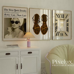 May include: Three framed wall art prints. The first features a vintage newspaper headline that reads "Better Late Than Ugly." The second shows a pair of leopard print sandals. The third print has a clock design. A small lamp and a white cabinet are in the foreground.
