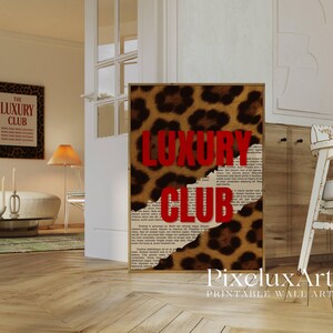 May include: A framed print with a leopard print background and the words "LUXURY CLUB" in red. The print has a torn paper effect, revealing a newspaper-style background. The image is in a room with other framed art and furniture.
