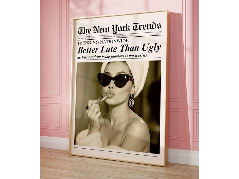 May include: A framed sepia-toned print featuring a woman applying lipstick, wearing sunglasses and a towel on her head. The print is designed to look like a newspaper, with the headline "The New York Trends" and the text "Better Late Than Ugly".