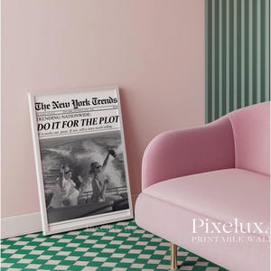 May include: A framed black and white print titled "The New York Trends" with the headline "DO IT FOR THE PLOT." The image shows people on a boat. A pink armchair with gold legs sits next to the print. The background is pink and green.
