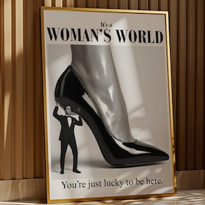 May include: Framed art print with a gold border. The image features a giant black high-heeled shoe with a man in a tuxedo holding it up. The text reads "It's a WOMAN'S WORLD" and "You're just lucky to be here."