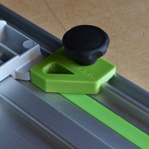 May include: A green plastic woodworking jig with a black knob. The jig has the word "T-Track" printed on it.