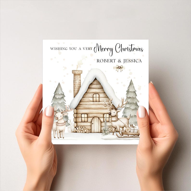 K&ouml;nnte beinhalten: Weihnachtskarte mit einer Aquarellillustration eines schneebedeckten Blockhauses, zwei Rentieren und Tannenb&auml;umen. Die Karte tr&auml;gt die Aufschrift "Wishing you a very Merry Christmas" und die Namen "ROBERT & JESSICA".