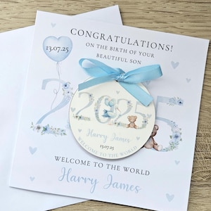 May include: A baby announcement card with a blue ribbon and a circular tag. The card says "Congratulations! On the birth of your beautiful son." The tag has the name "Harry James" and the date "13.07.25". A teddy bear and stork are also featured.