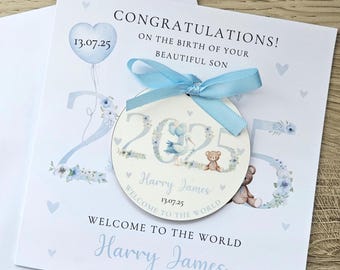 Può includere: Biglietto di annuncio nascita con un nastro blu e un'etichetta circolare. Il biglietto dice "Congratulazioni! Per la nascita del tuo bellissimo figlio". L'etichetta riporta il nome "Harry James" e la data "13.07.25". Sono presenti anche un orsacchiotto e una cicogna.