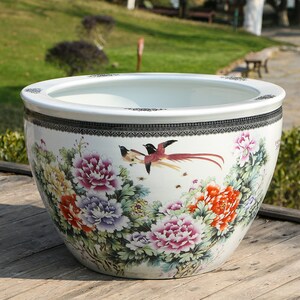 May include: A large, white ceramic planter with a wide rim and a detailed floral and bird design. The planter features colourful peonies and birds with long tail feathers. The rim has a black and white patterned border.