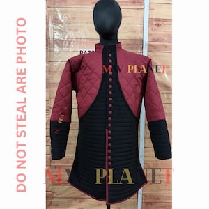 Puede incluir: Gambesón medieval acolchado burdeos y negro exhibido en un maniquí. El gambesón presenta un cuello alto, cierres de botones y acolchado con diseño de diamantes en las secciones burdeos. Las mangas y la parte inferior son negras.