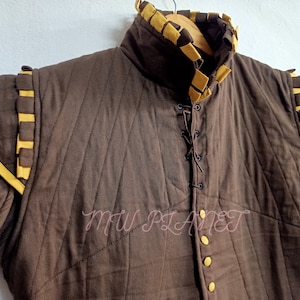 May include: A brown quilted jacket with yellow trim and a lace-up front. The jacket has a high collar and is lined with a brown fabric. The jacket is made of a thick, durable material and is perfect for keeping warm in cold weather.
