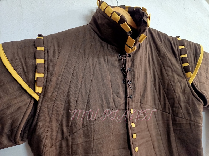 May include: A brown quilted jacket with yellow trim and a lace-up front. The jacket has a high collar and is lined with a brown fabric. The jacket is made of a thick, durable material and is perfect for keeping warm in cold weather.