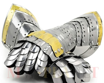 May include: Pair of medieval gauntlets made of polished steel with brass accents. The gauntlets feature articulated finger plates and wrist protection, with a scalloped edge design. The metal armor is designed to protect the hands and wrists.