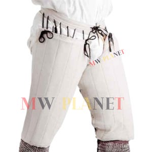 May include: White padded leg armor with black straps and laces. The armor is quilted and has a medieval design. The text "MW PLANET" is visible on the image.