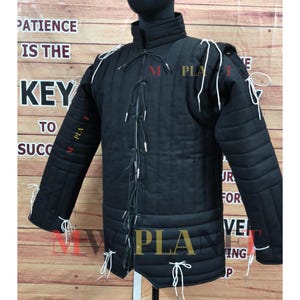 May include: Black padded jacket with white ties and stitching details. The jacket has a high collar and is designed for protection. The text "PATIENCE IS THE KEY TO SUCC" is visible on the background.
