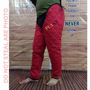 May include: Red quilted leg armor with a black leather trim and a drawstring closure. The armor is worn by a person standing on a wooden floor. The text "DO NOT STEAL ARE PHOTO" is visible on the left side of the image. The text "PLANE" is visible on the right side of the image.