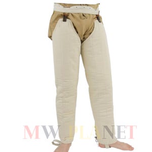 May include: White padded medieval leg armor with a brown leather belt and buckles. The armor is made of linen and has a quilted design. The armor is tied at the bottom with laces.