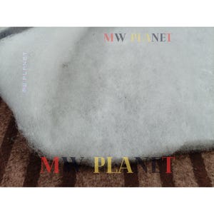 May include: Close-up of a white, fluffy material, possibly batting or stuffing, with a textured appearance. The material is layered over a brown and tan striped fabric. The text "MW PLANET" is visible in the image.
