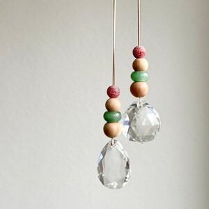 May include: Two crystal suncatchers with wooden and green beads hanging from white strings. The suncatchers are teardrop shaped and have a faceted design.