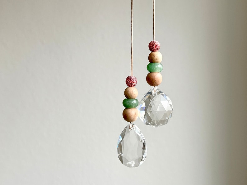 May include: Two crystal suncatchers with wooden and green beads hanging from white strings. The suncatchers are teardrop shaped and have a faceted design.