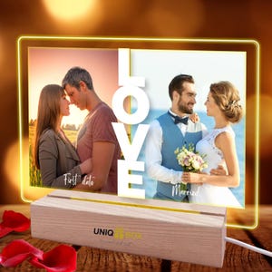 May include: A lighted photo frame with two images of a couple, one from their first date and the other from their wedding day. The word "LOVE" is in large white letters. The frame sits on a wooden base with the text "UNIQ it BOX".