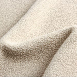 Puede incluir: Primer plano de una tela suave de color crema con una textura peluda. La tela est&aacute; hecha de un material afelpado que es perfecto para una manta o una manta acogedora.