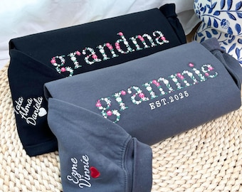 Könnte beinhalten: Drei gefaltete Sweatshirts in Schwarz und Grau, bestickt mit floralem Text. Das schwarze Sweatshirt trägt die Aufschrift "grandma" und das graue "grammie EST. 2025". Zusätzliche Namen sind auf den Ärmeln gestickt.