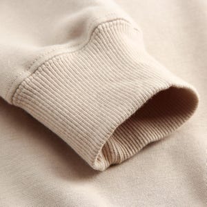 Puede incluir: Primer plano del pu&ntilde;o acanalado beige de una sudadera de manga larga.
