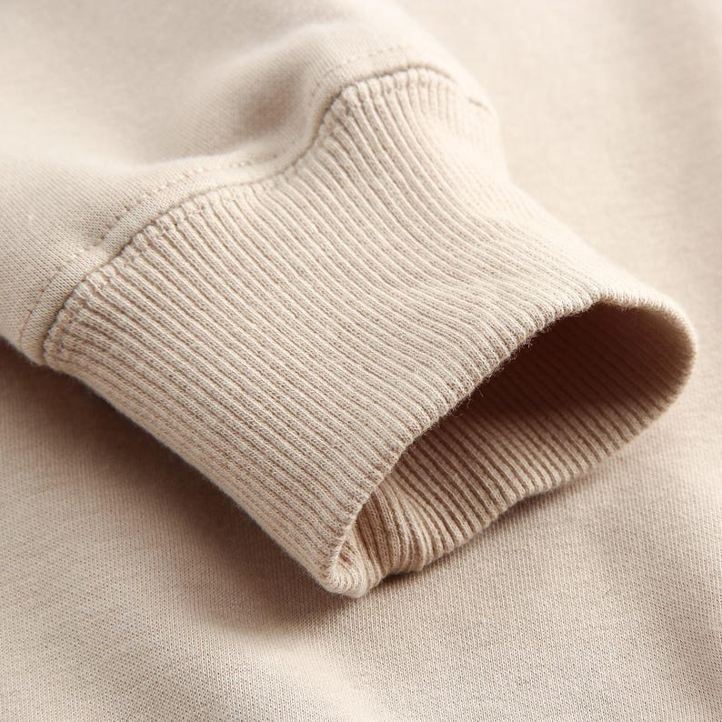 Puede incluir: Primer plano del pu&ntilde;o acanalado beige de una sudadera de manga larga.