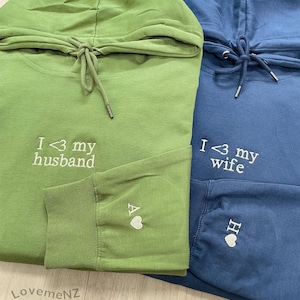 Peut inclure: Deux sweat-shirts à capuche, l'un vert et l'autre bleu, avec des messages brodés. Le sweat-shirt vert dit "I <3 my husband" et le sweat-shirt bleu dit "I <3 my wife".