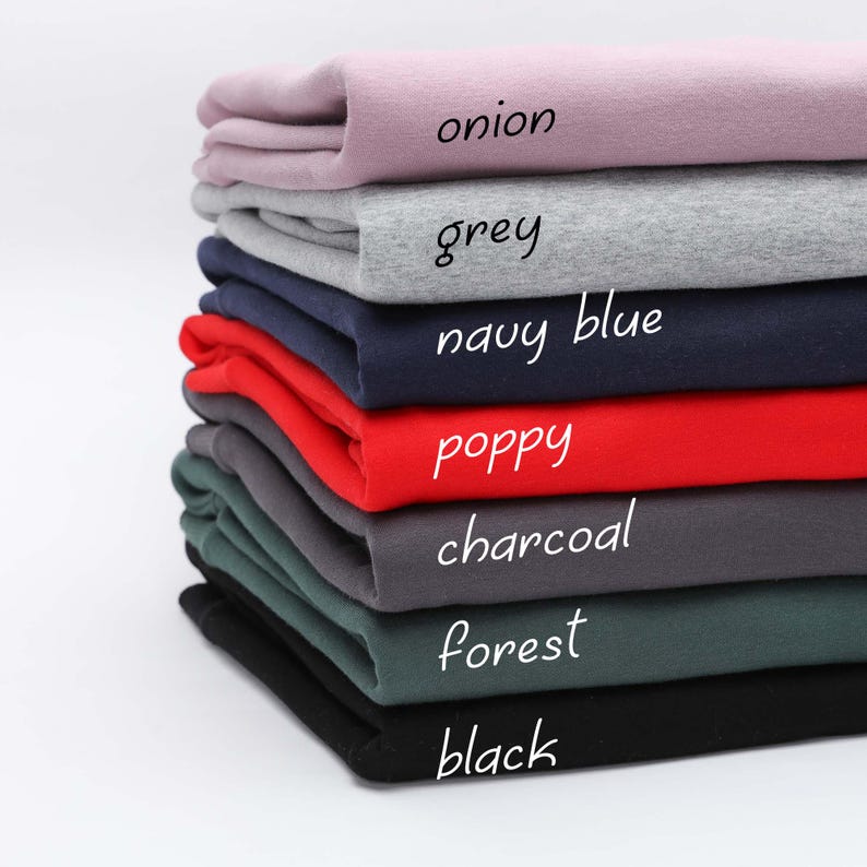 Puede incluir: Una pila de ocho camisetas dobladas en diferentes colores, incluyendo cebolla, gris, azul marino, amapola, carb&oacute;n, bosque y negro.