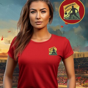 May include: A red t-shirt with a small embroidered patch on the left chest. The patch is a yellow, green, and brown circle with the text "Unbreakable Wall Stand Tall" and a silhouette of a person playing football.