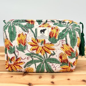 May include: A quilted cosmetic bag with a floral pattern of yellow and red flowers, green leaves, and a white background. The bag has a green tassel and a label that says "THE INDIAN ELEPHANT".