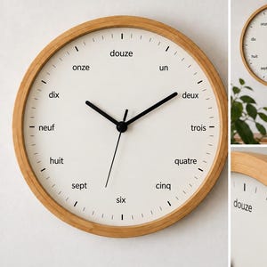 May include: A round wall clock with a light wood frame and a white face. The dial features black hour markers and black hands. Instead of numbers, the hours are written in French words from un to douze, arranged in a circular pattern on the face.