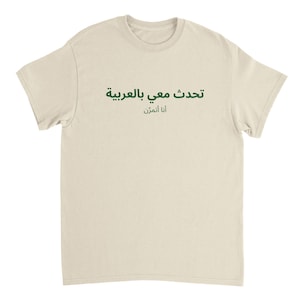 Puede incluir: Una camiseta color crema con texto árabe verde. El texto dice "Háblame en árabe" y "Estoy aprendiendo". La camiseta tiene cuello redondo y mangas cortas.