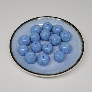 Op de afbeelding: Een verzameling van 15 ronde kralen in lichtblauw en groen met een swirl-patroon in een blauwe en witte keramische schaal.