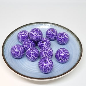 Op de afbeelding: Een verzameling van paarse en witte swirl-patroon kralen op een blauw bord.