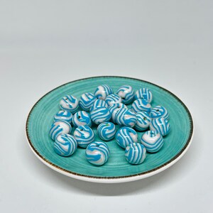 Op de afbeelding: Een stapel blauwe en witte kralen met een swirl-patroon op een turquoise bord.