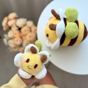 K&ouml;nnte beinhalten: Zwei handgefertigte H&auml;keltiere: eine gelb-braune Biene mit wei&szlig;en Fl&uuml;geln und gr&uuml;nen Akzenten und eine gelbe Blume mit wei&szlig;en Bl&uuml;tenbl&auml;ttern und braunen Akzenten. Die Spielzeuge sind weich und kuschelig, perfekt f&uuml;r Kinder.