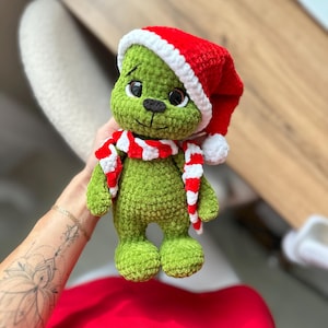 Peut inclure: Une peluche crochet&eacute;e verte avec de grands yeux sombres et un nez noir. La figurine porte un bonnet de P&egrave;re No&euml;l rouge et blanc avec un pompon blanc et une &eacute;charpe ray&eacute;e rouge et blanche assortie. La texture du fil est douce et duveteuse.