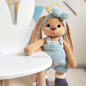 May include: A tan crocheted rabbit plush toy with long ears, wearing a light blue headband with a bow, light blue overalls with small buttons, and dark gray boots with white cuffs. The text PARKAEVA_HM is visible on the rabbit's chest.