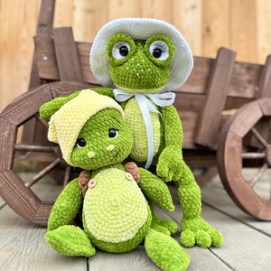 Puede incluir: Dos peluches de rana verdes hechos de hilo suave. La rana m&aacute;s grande lleva un sombrero de ganchillo blanco con una cinta blanca atada bajo la barbilla y tiene pesta&ntilde;as largas. La rana m&aacute;s peque&ntilde;a lleva un gorro de ganchillo amarillo y botones.