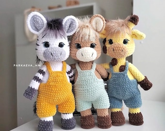 May include: Three crocheted stuffed animals: a zebra with black and white stripes wearing yellow overalls, a brown and white giraffe wearing blue overalls, and a brown and white horse wearing light blue overalls.