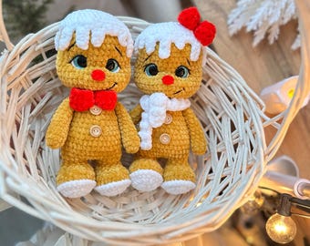 May include: Two crocheted gingerbread man dolls in a white wicker basket. The dolls have yellow bodies, white frosting-like hair, and red bow ties. One doll has a white scarf and a red bow. The dolls have button eyes and are a festive holiday decoration.