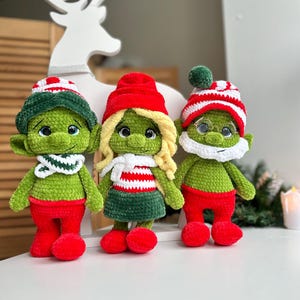 Puede incluir: Tres gnomos navideños de crochet hechos a mano. Cada gnomo tiene un cuerpo verde, pantalones y zapatos rojos, y un sombrero a juego. Un gnomo tiene un sombrero a rayas blancas y verdes, otro tiene un sombrero rojo y el tercero tiene un sombrero a rayas blancas y rojas.