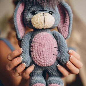 Pu&ograve; includere: Un giocattolo di peluche a forma di asino, realizzato a uncinetto. L'asino &egrave; blu e grigio con dettagli rosa. Ha una criniera marrone e soffice e un viso bianco con occhi neri.