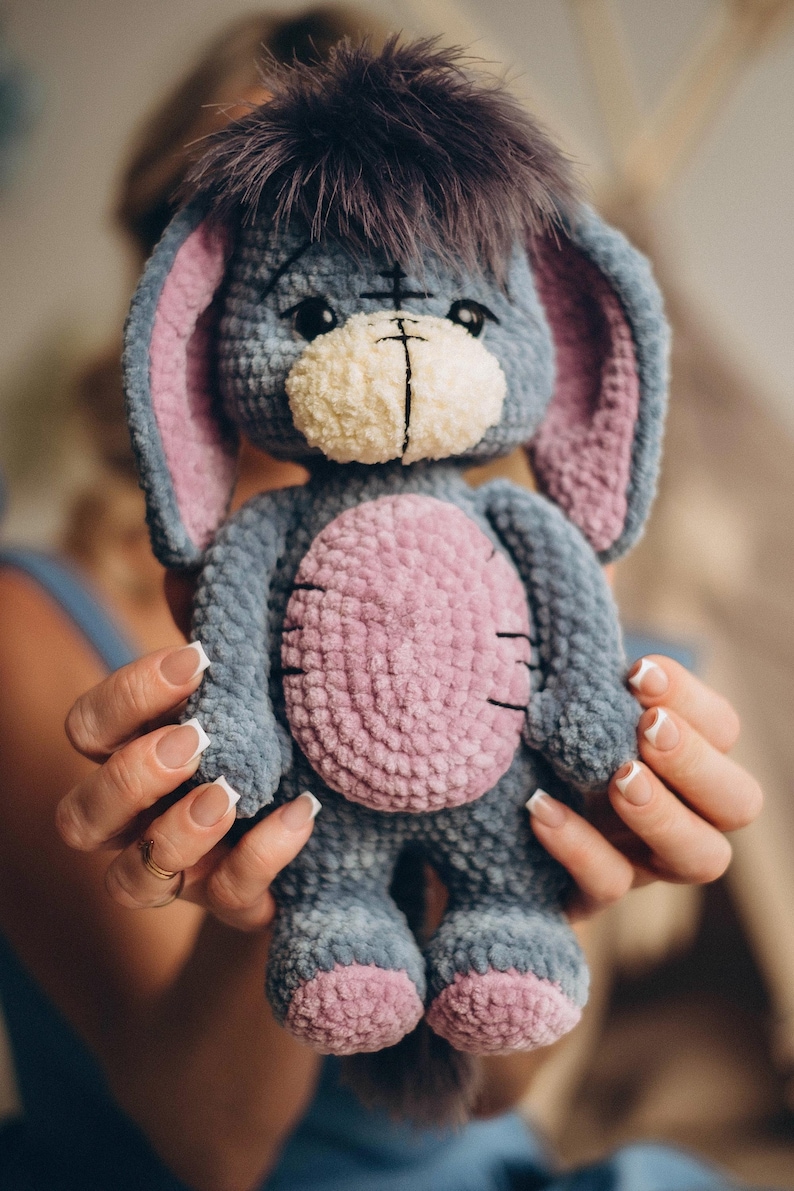 Pu&ograve; includere: Un giocattolo di peluche a forma di asino, realizzato a uncinetto. L'asino &egrave; blu e grigio con dettagli rosa. Ha una criniera marrone e soffice e un viso bianco con occhi neri.