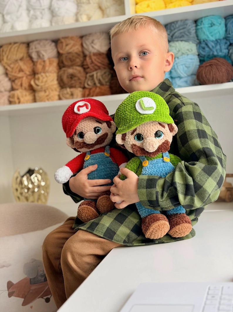 May include: Two handmade crochet plush dolls representing Mario and Luigi. Mario wears a red hat with a white M, a red shirt, and blue overalls. Luigi wears a green hat with a white L, a green shirt, and blue overalls. Both have brown mustaches.