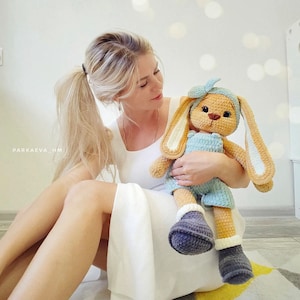 May include: A crocheted stuffed rabbit toy with long ears, wearing a light blue romper, a matching headband with a bow, and dark gray boots with white cuffs. The rabbit has a tan body, dark eyes, and a brown stitched nose. Text reads PARKAEVA_HM.