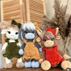 May include: Three crocheted stuffed animals: a white lamb with green overalls, a gray donkey with a yellow dress, and a brown cow with a red dress.